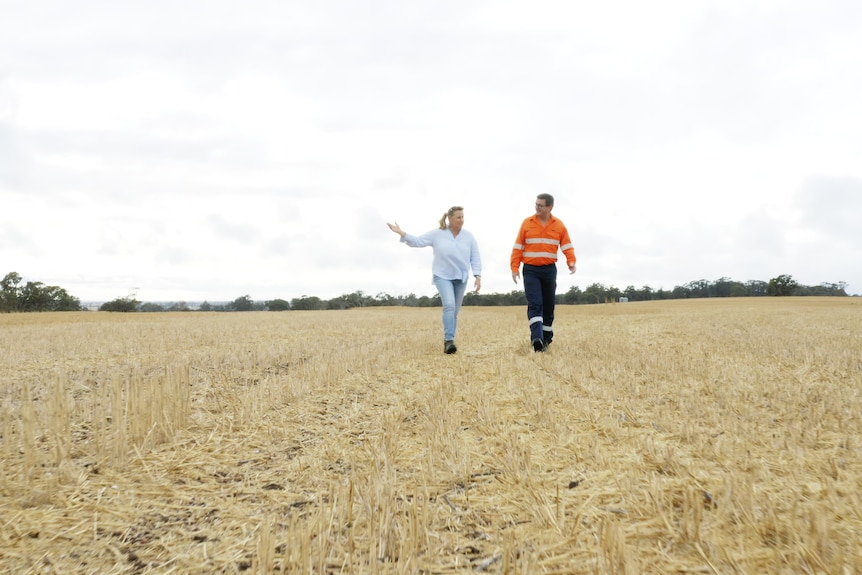 A man in high-vis and a woman in light-coloured clothes stand in a large field.