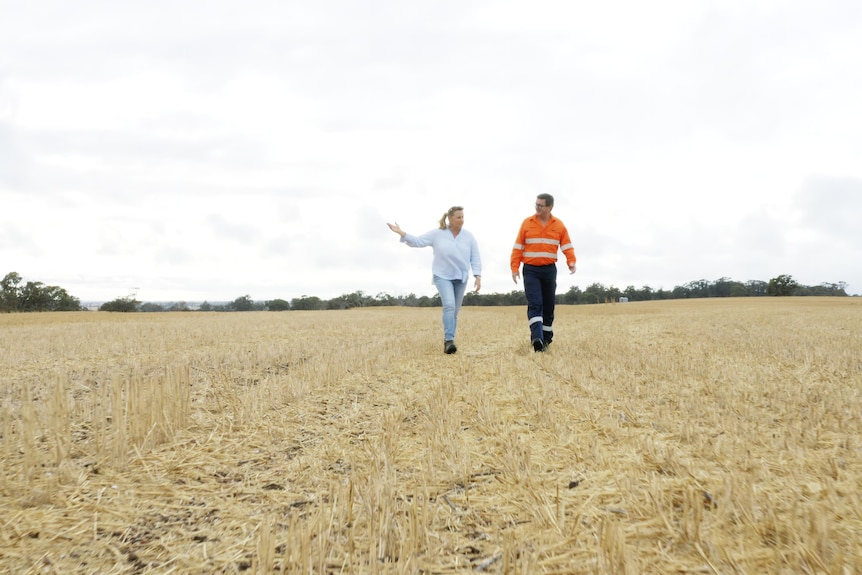 A man in high visibility and a woman in light clothing stand in a large field.