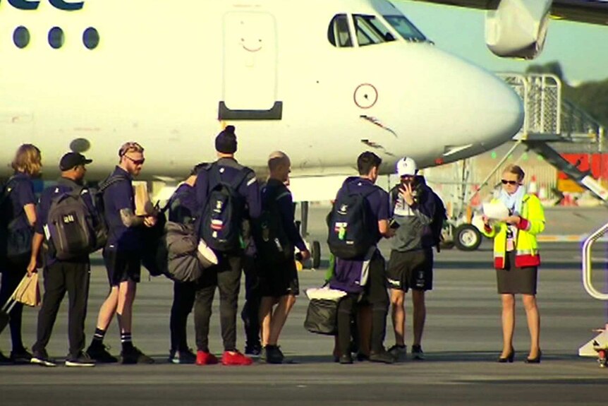 Nine Dockers players stand at the foot of a staircase to a plane.