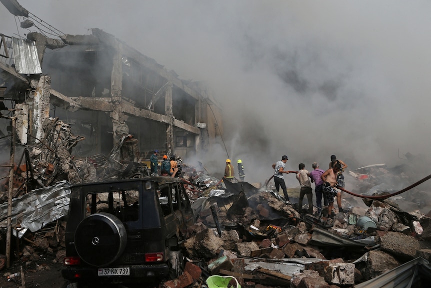 People help firefighters to extinguish a fire near a smoldering building