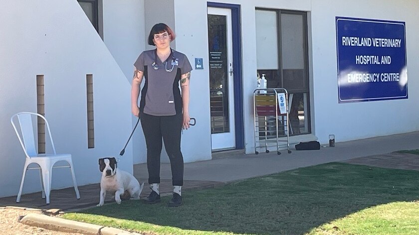 A veterinarian stands in front of the Riverland Veterinary Practice with a dog on a leash