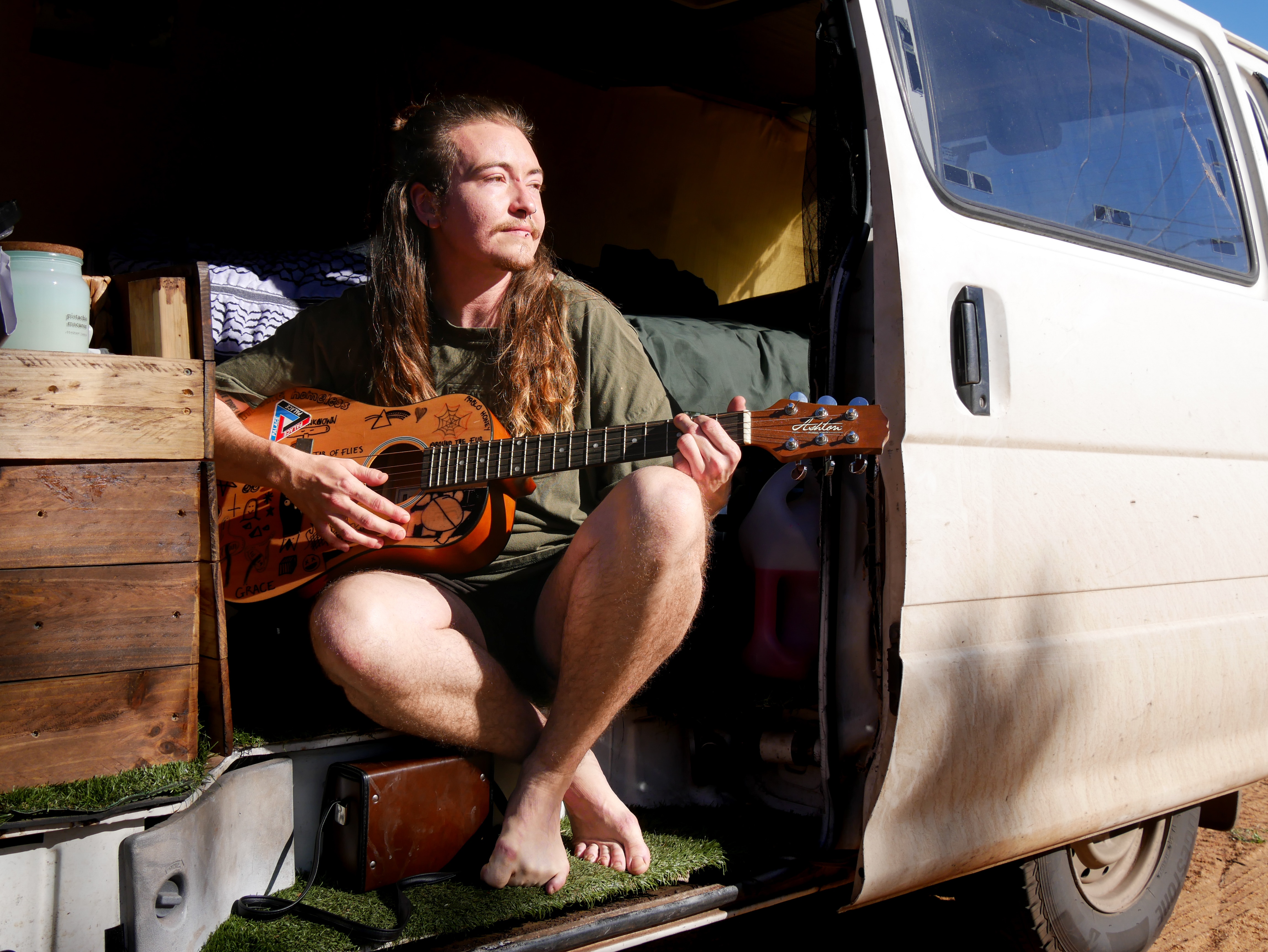Johnathan sitting in his van playing a guitar looking out into the distance.