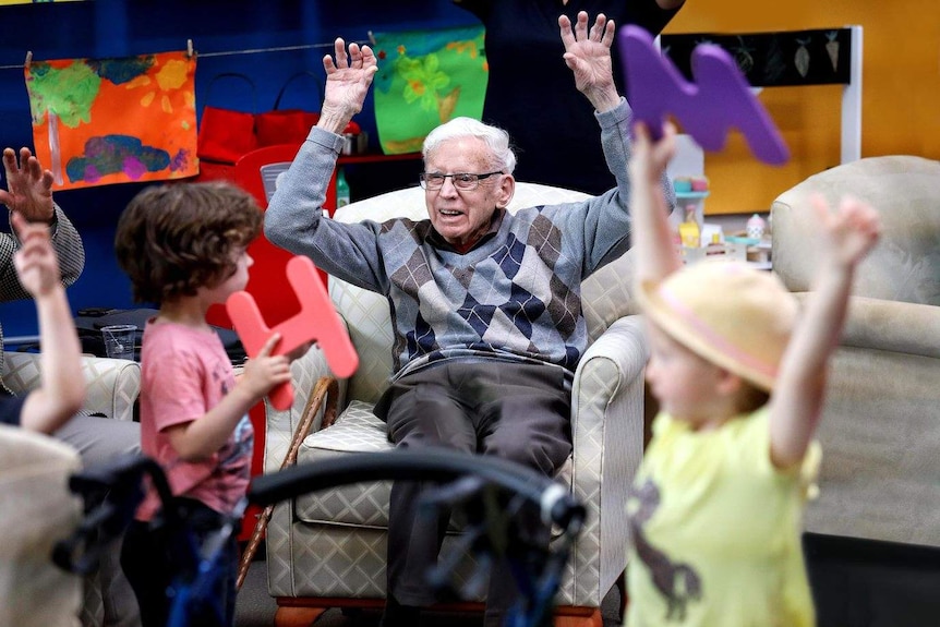three children wave colourful letters in the air around an elderly man smiling and waving