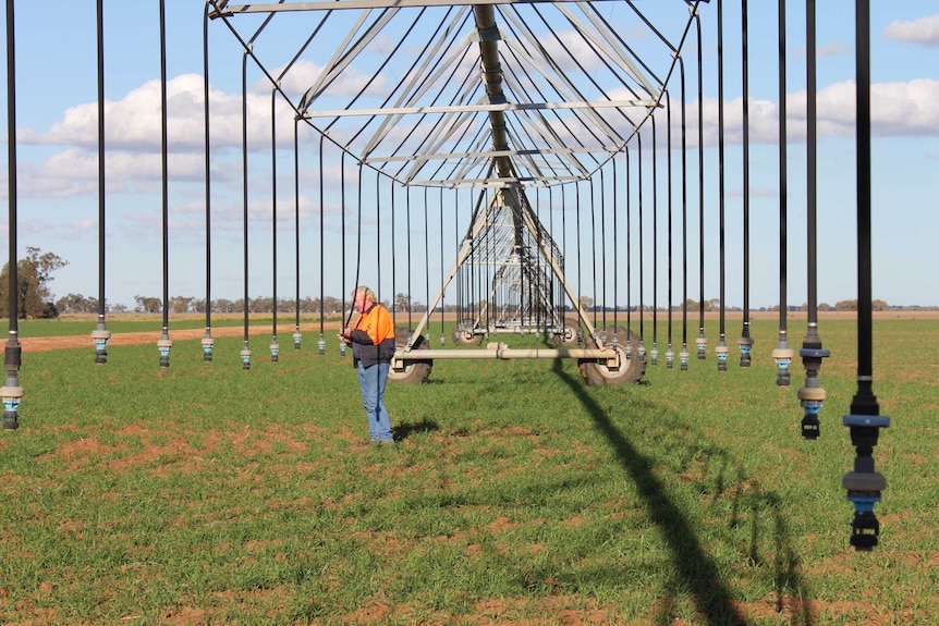 A man in an orange jacket checking nozzles on a lateral irrigator.