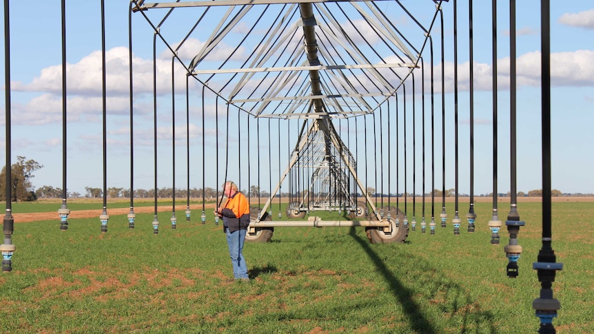 A man in an orange jacket checking nozzles on a lateral irrigator.