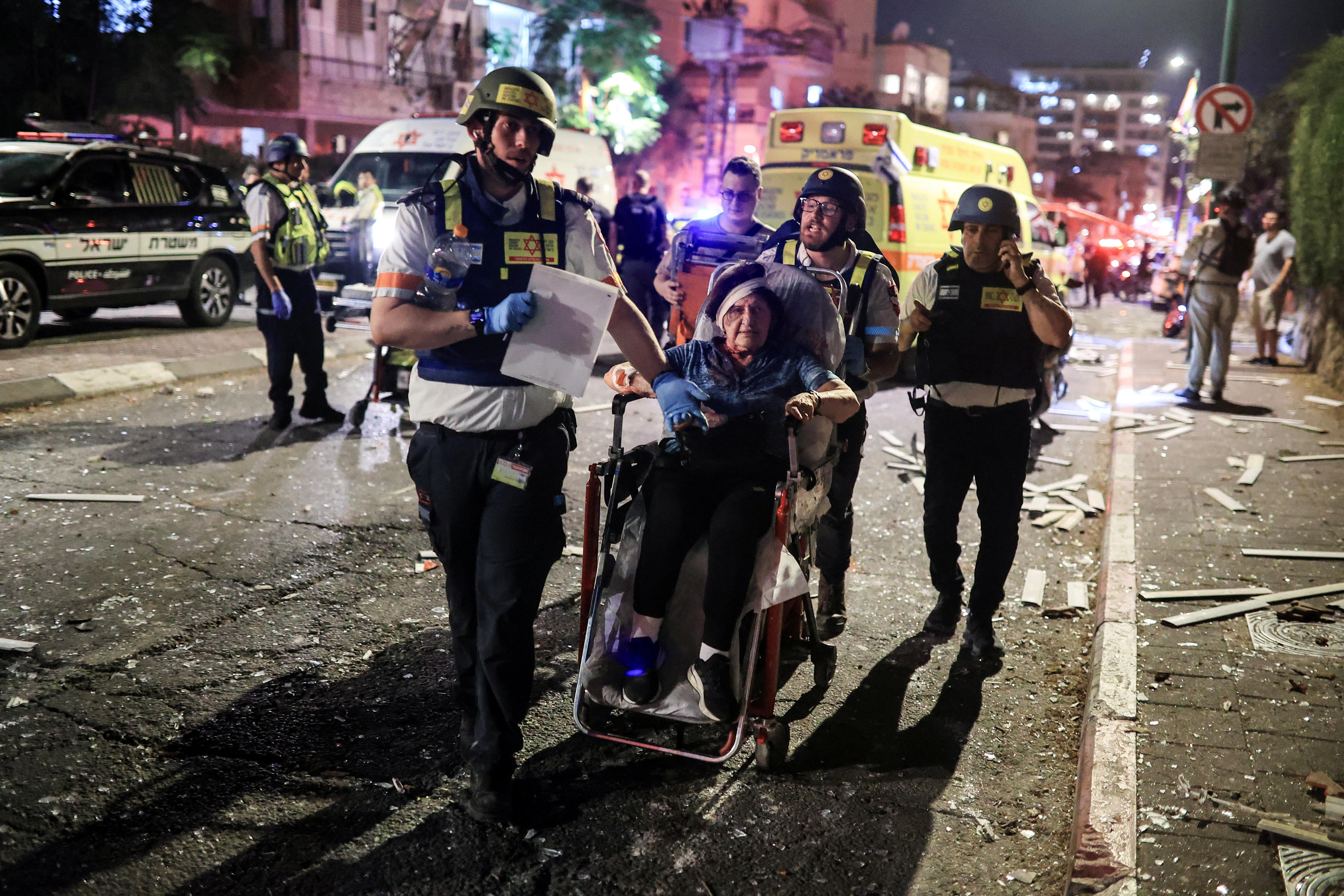 A woman with a bandaged head is wheeled down a street by paramedics.