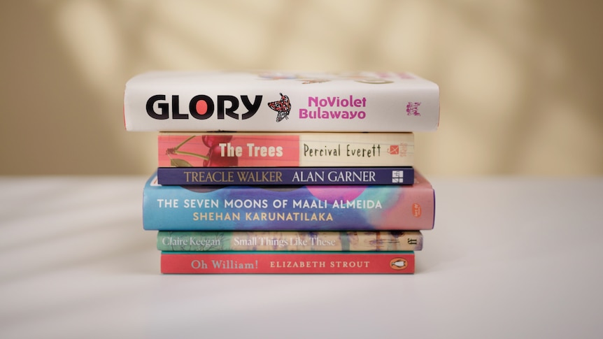 A stack of six books, of various sizes and lengths, as well as different colours, such as red, white and navy