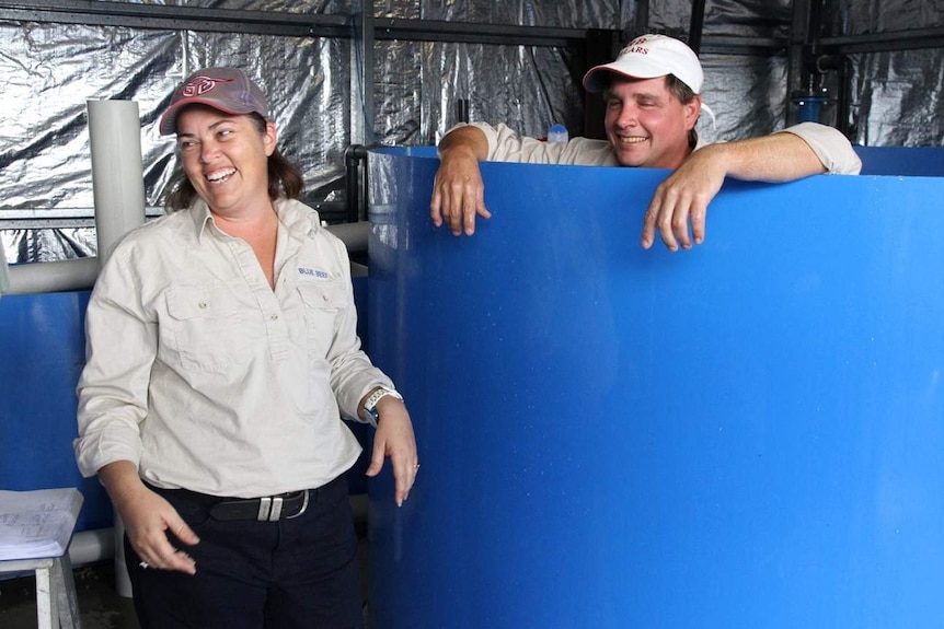 Woman laughing and man with eyes shut stands in a blue tank that comes to his chin.