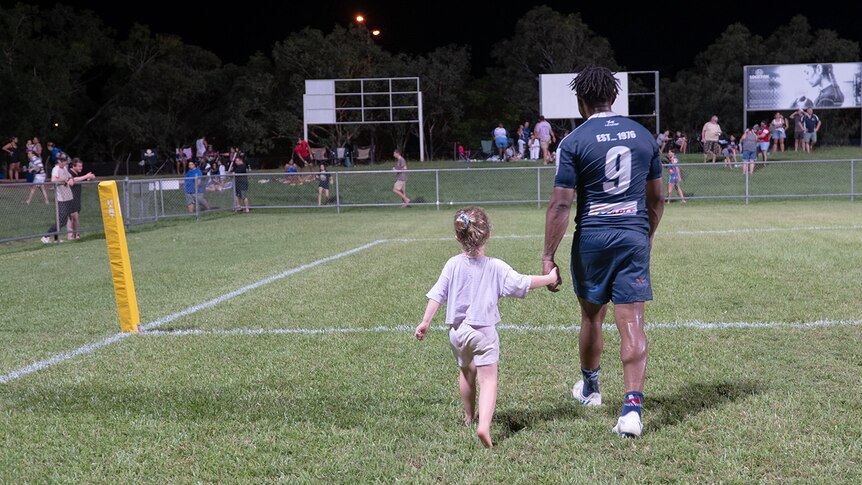 A man with a number 9 on his shirt walks hand in hand with a child with backs to the camera