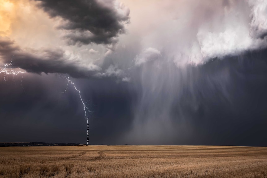 Lightning strikes from dark clouds above a rural landscape.