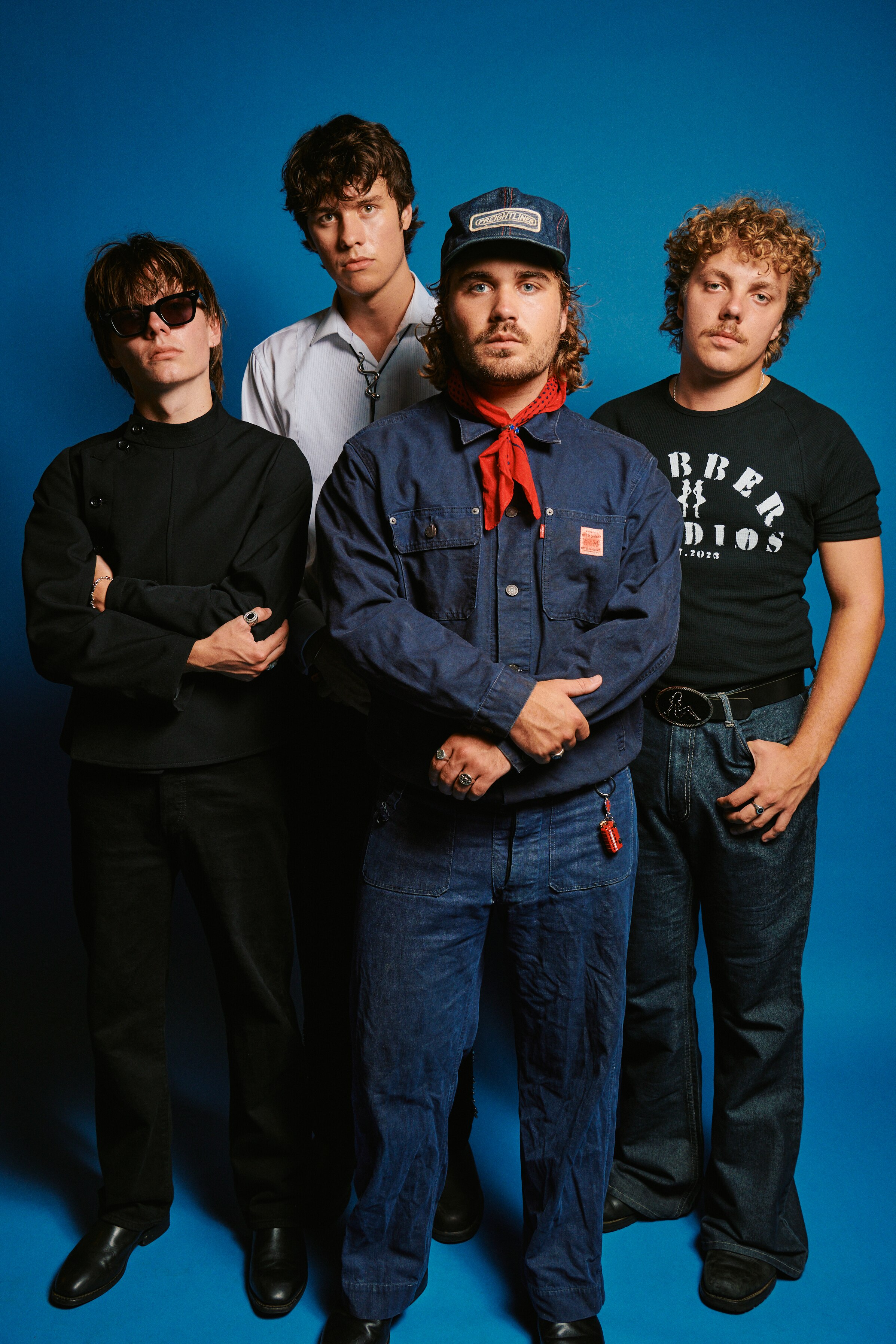Four men stand together with solemn faces on a blue backdrop