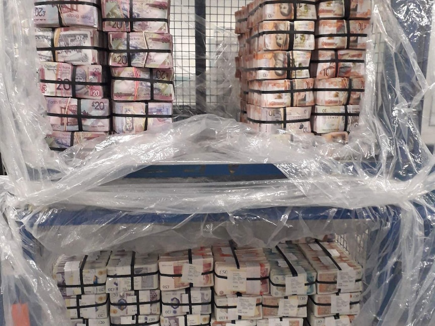A crate of cash stacked high and covered in plastic.