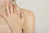 A picture of a woman with her hand on the front left part of her neck and shoulder - over the collarbone