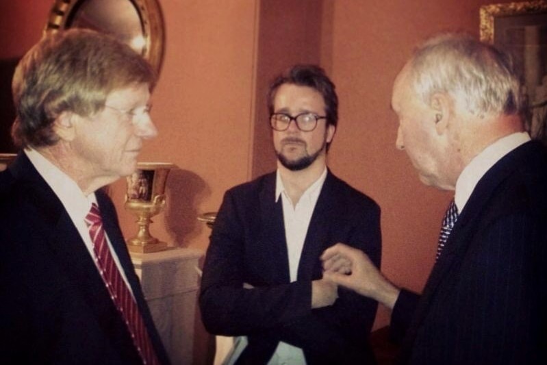 Man with a beard and arms crossed standing between two men looking at each other.