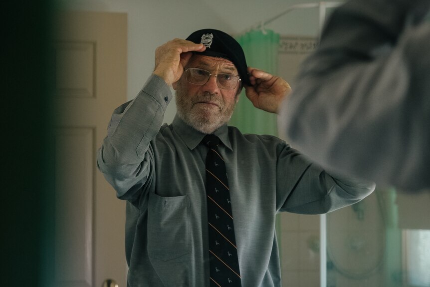 A man places his hat on his head in the mirror.