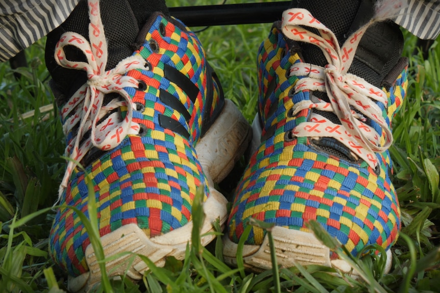 Red, yellow, blue and green chequered shoes on grass with white laces that have a red ribbon pattern.