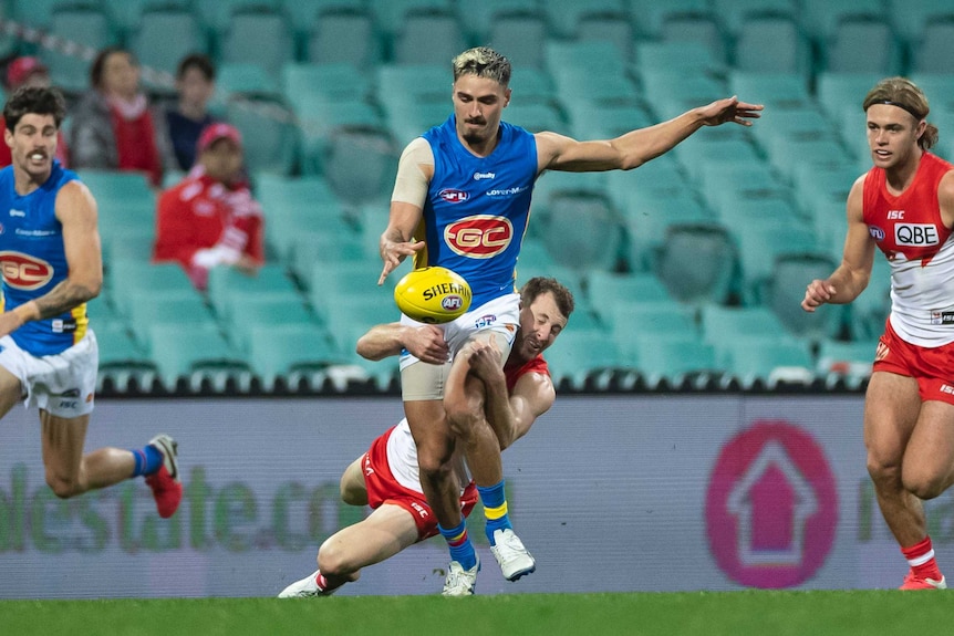 Gold Coast Suns' Izak Rankine tries to kick the ball as Sydney Swans' Harry Cunningham tackles him around the thighs.
