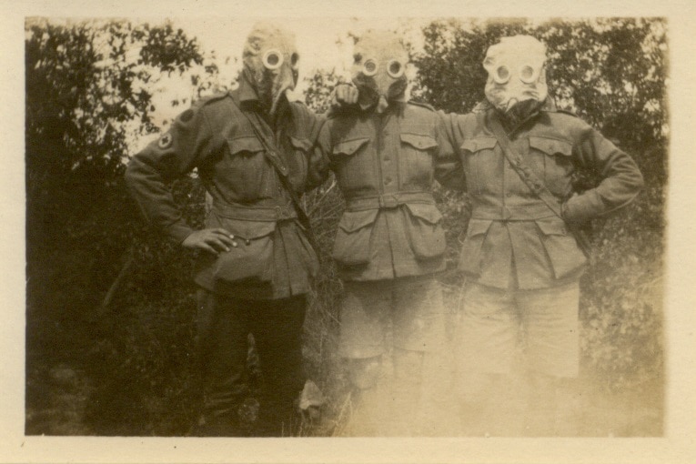 Sepia photo of three soldiers with arms around each other, wearing gas masks