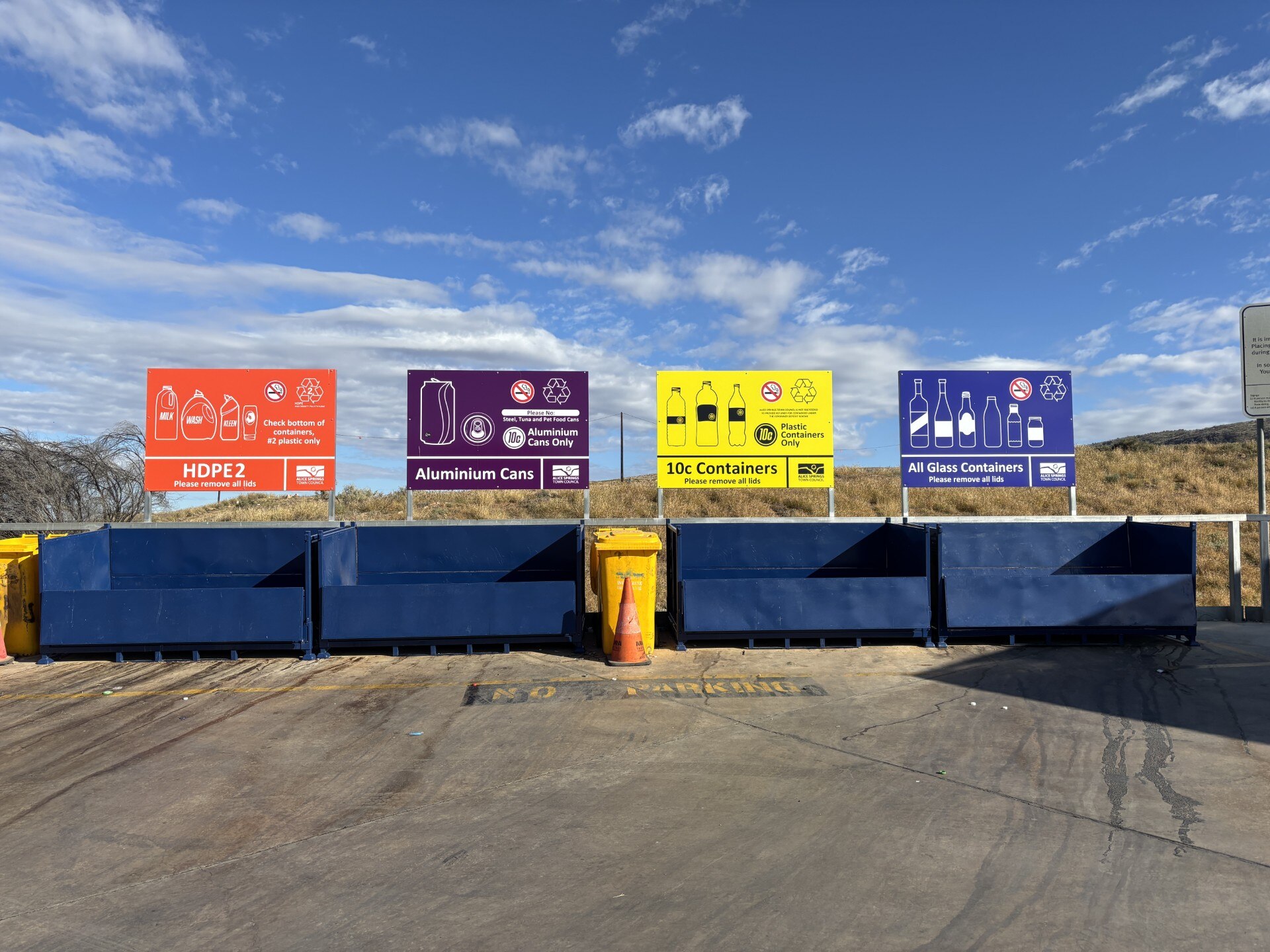 Red, purple, yellow and blue signs sit about four blue skip bins.