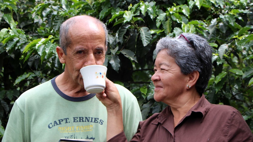 A woman holding a cup that a man is drinking from