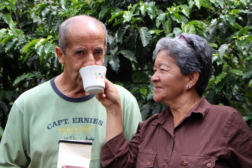 A woman holding a cup that a man is drinking from