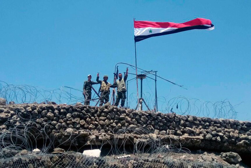Syrian troops flash the victory sign next to the Syrian flag in Tell al-Haara