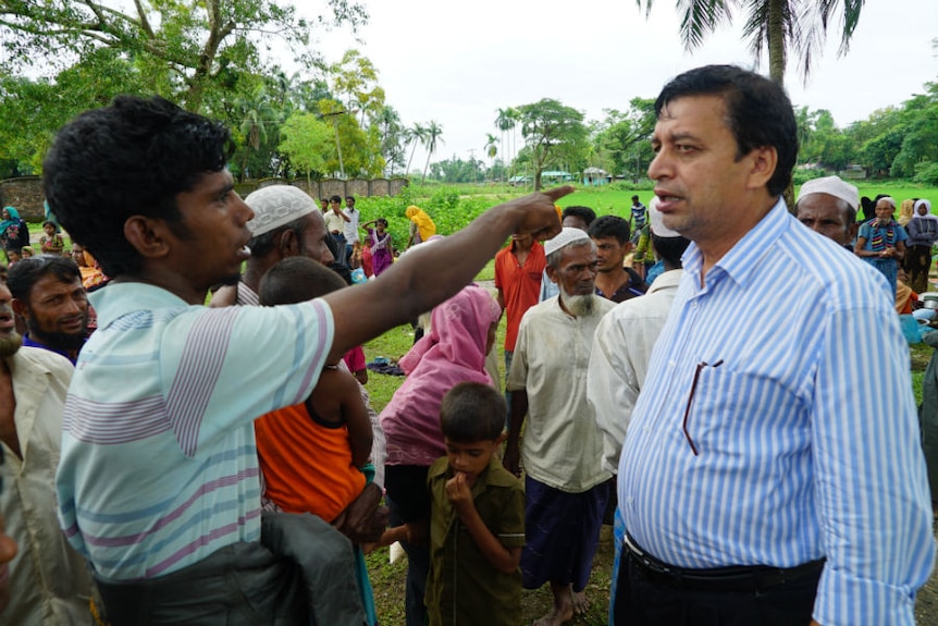 A man in a business shirt speaks to a refugee as others look on.