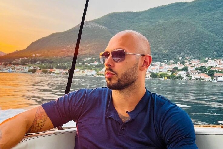 Man wearing sunglasses sits in boat staring out at water with serious expression. 