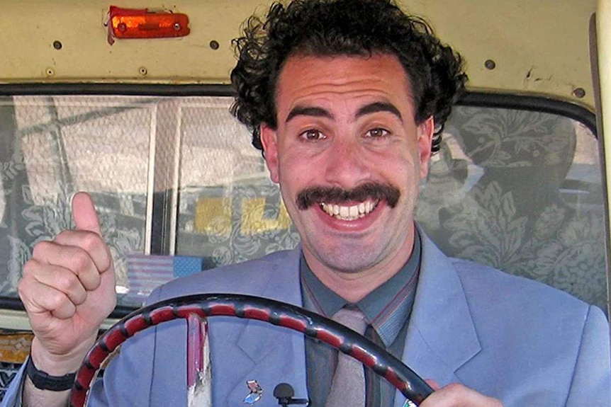 Borat gives a thumbs up and smiles for the camera