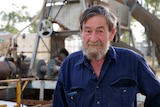 Murray looking at the camera wearing dark blue collared shirt, machinery blurred out in background.