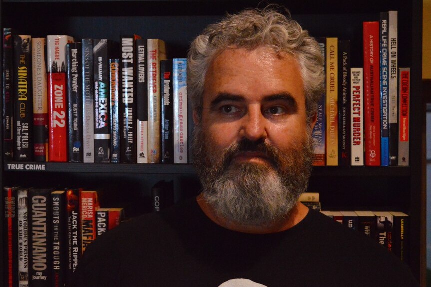 Portrait picture of Paul Morgan, in front a book shelf filled with books, looking away from the camera.