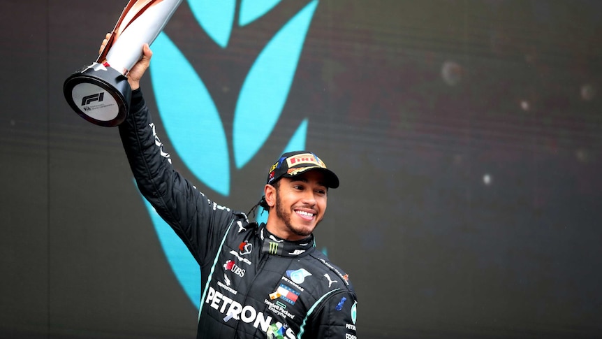 Lewis Hamilton lifts a trophy and smiles