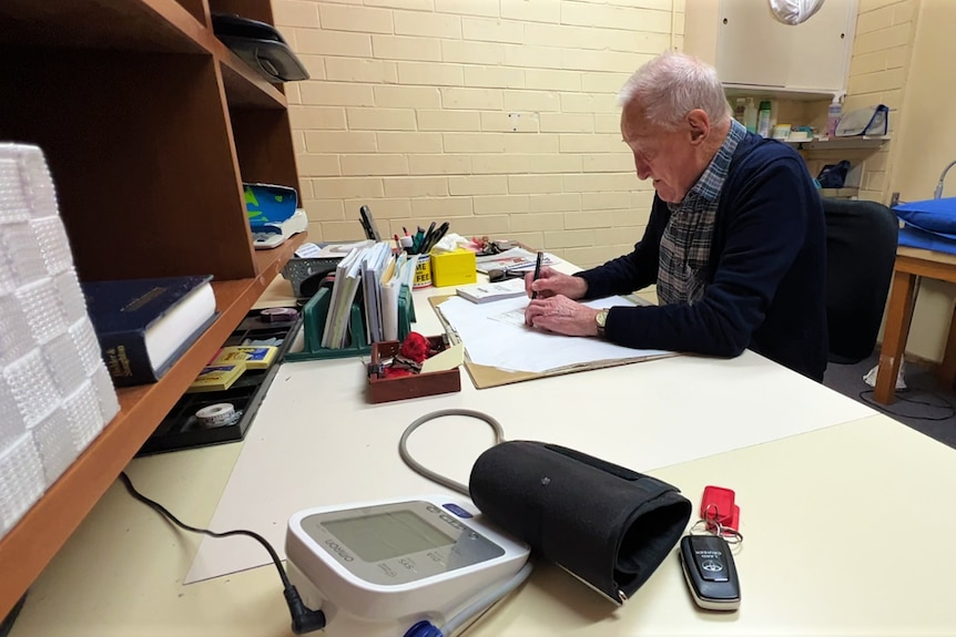 He sits at a desk and writes in a white-brick walled office