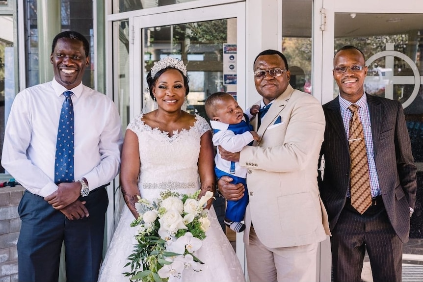 South Sudanese bride and groom standing in the middle with two other men on either side.