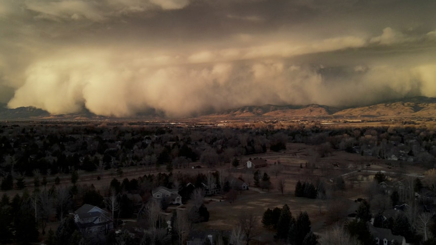 A large cloud of dust sweeps down from a mountain range over a town. 