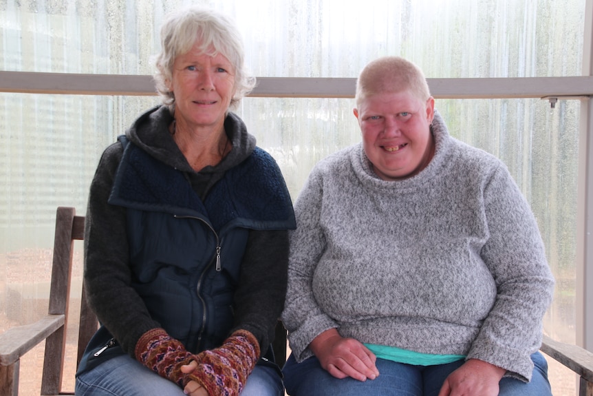 A woman with short gray hair sits beside another woman wearing a grey jumper, smiling