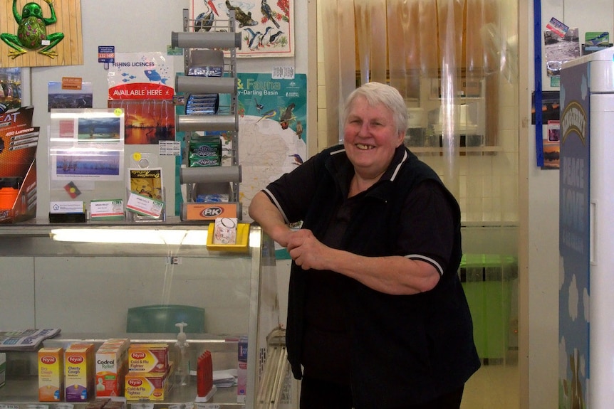 A woman in a black shirt leans on a glass cabinet piled with confectionary and items.