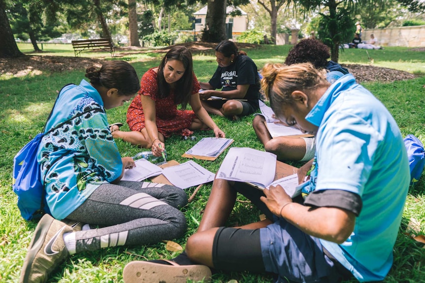 A group of people sitting on grass reading.