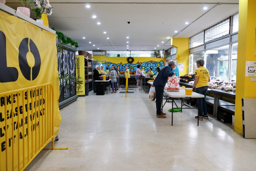 A room with yellow walls and fold-out tables with food on them staffed by people in yellow t-shirts