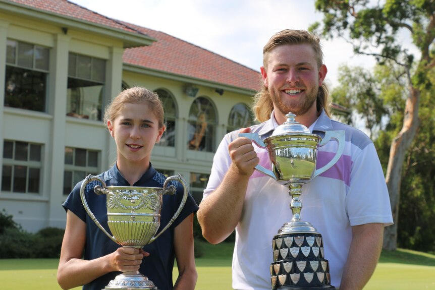 A 12-year-old woman and a young man both hold trophies on a golf course.