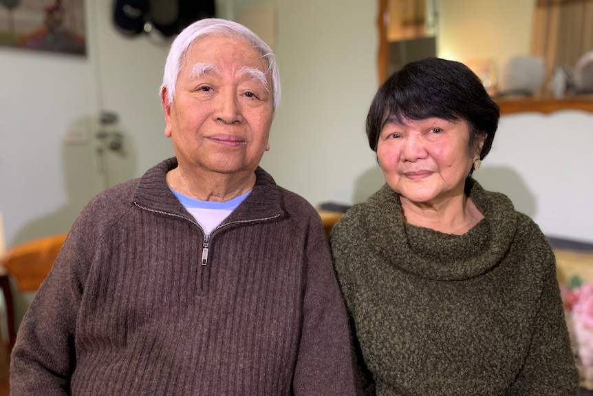 A portrait of Rodolfo and Erlinda sittig together wearing warm clothing in their home in Melbourne.