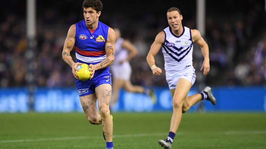 A Western Bulldogs player runs with the ball as a Fremantle Dockers play struggles to catch him.