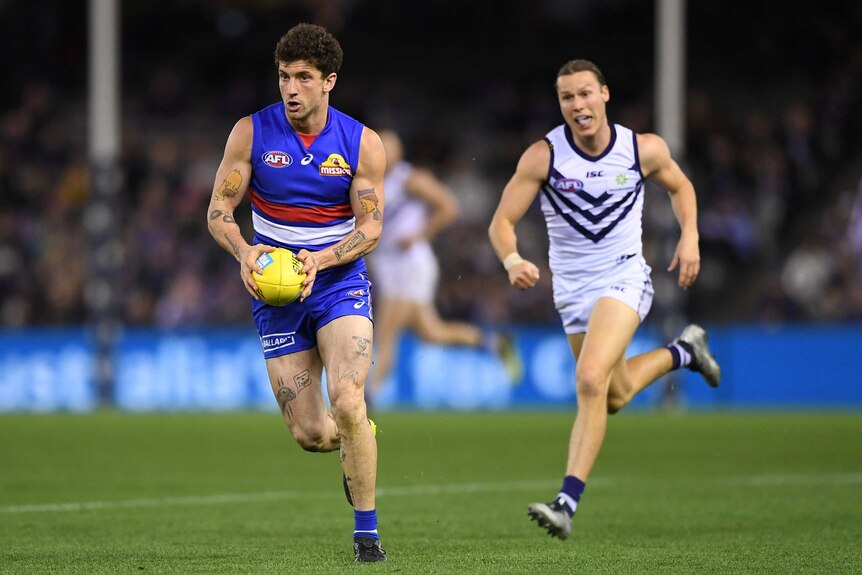 A Western Bulldogs player runs with the ball as a Fremantle Dockers play struggles to catch him.