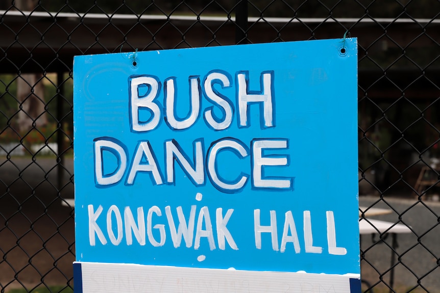 Blue sign with white writing affixed to a fence advertising a Bush Dance in the Kongwak Hall