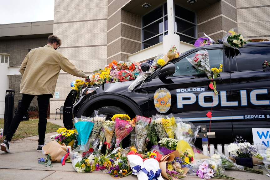 A man leaves a bouquet on a police cruiser parked outside the Boulder Police Department.