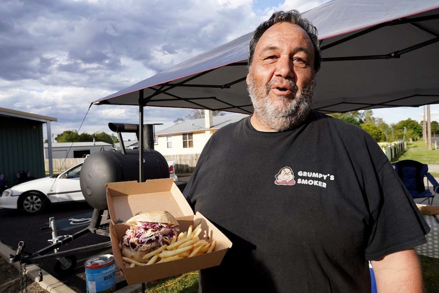 Stuart Thomson smiles while holding a pulled pork burger he's assembled at a CFS fundraiser for Nangwarry in South Australia.