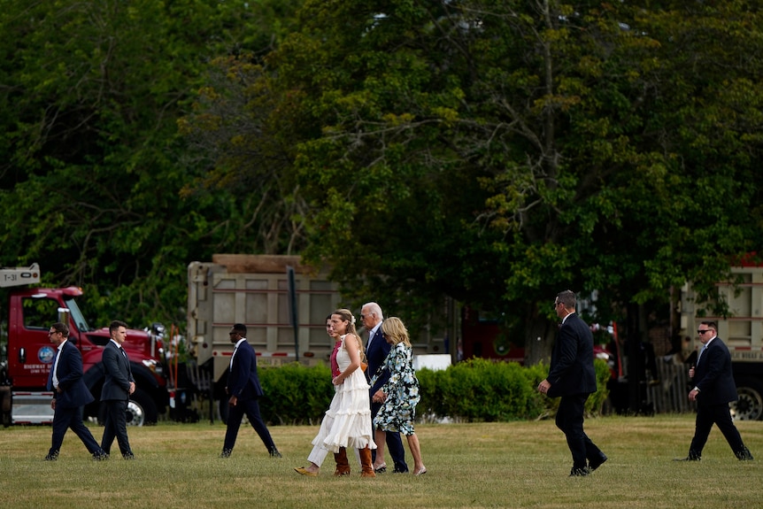 The biden family walking on a grassy area surrounded by security. 
