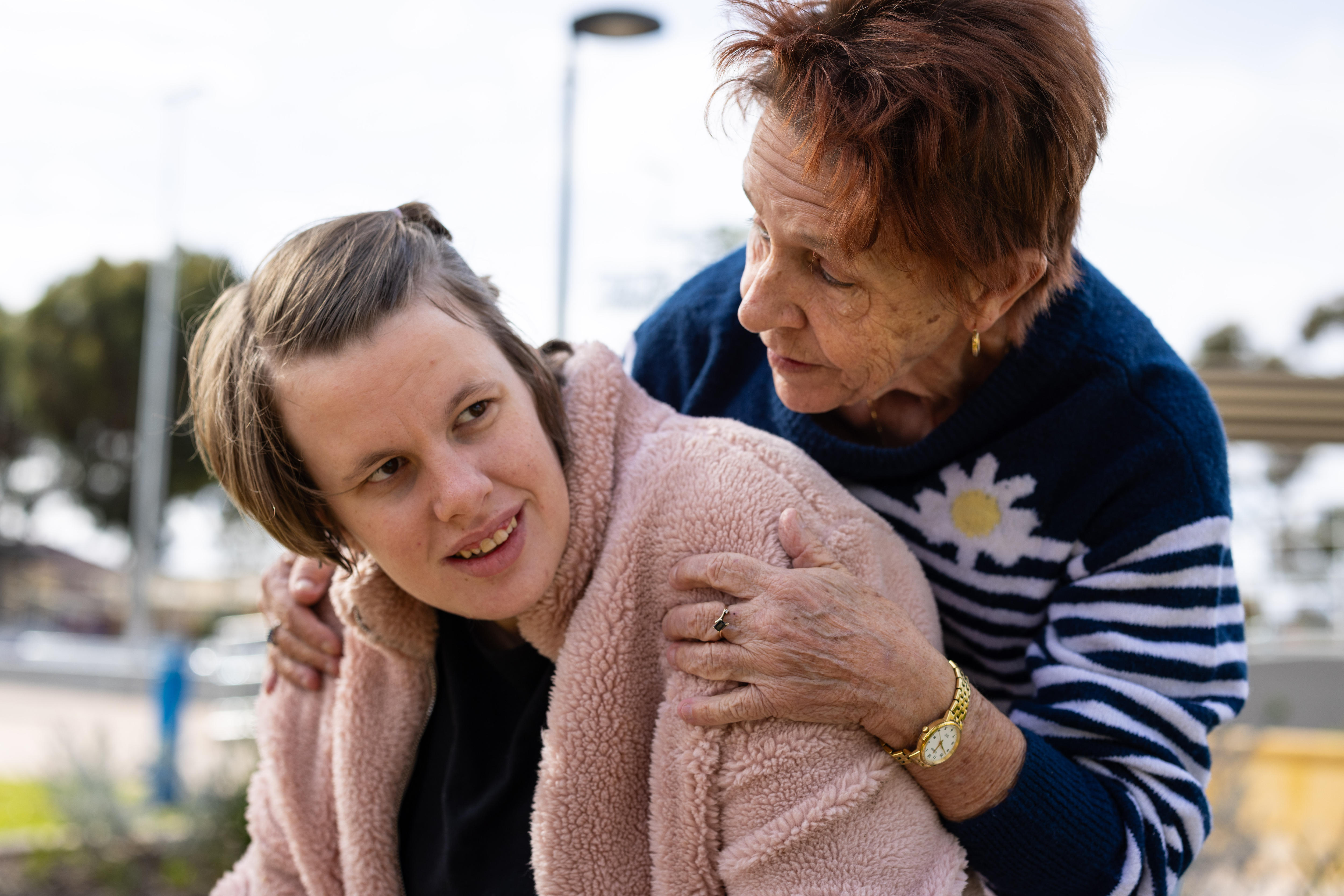 An older woman holding her adult daughter in a park