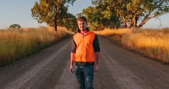 Artist Guido Van Helten wearing high-vis tee standing in middle of unsealed country road.