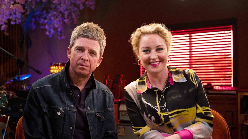 A middle-aged man in a denim jacket sits beside a smiling blonde woman with pink lipstick, both facing the camera.